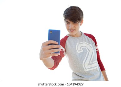 Portrait Of An Attractive Teenager Boy Holding His Smartphone With His Hand And Taking A Selfie Of Himself Against A Sunny Sky. Using Smart Phone Technology Outdoors To Take Photos.