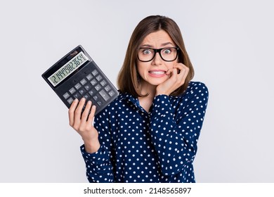 Portrait of attractive terrified nervous girl holding calculator bad balance biting nail isolated over grey pastel color background