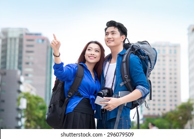 Portrait Of An Attractive Tourist Young Couple Relaxing Sightseeing And Visiting A Destination City On Holiday, Pointing Up And Enjoying Traveling Together, Outdoors. Tourism, Travel And Lifestyle.