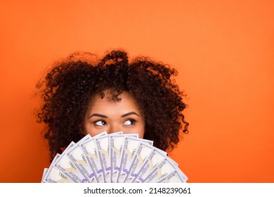 Portrait of attractive trendy funny mysterious girl holding cash hiding face isolated over bright orange color background Stock-foto