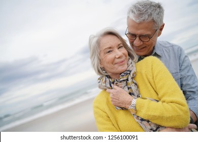 Portrait of attractive vibrant senior couple embracing on beach in fall                              