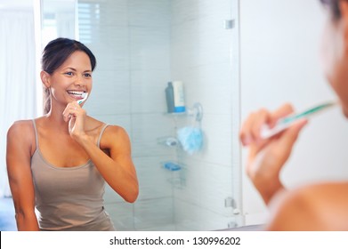 Portrait of attractive woman brushing teeth in bathroom and looking in the mirror at reflection. healthy teeth.