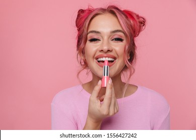 Portrait of attractive woman laughing and applying makeup with lipstick isolated over pink background - Powered by Shutterstock