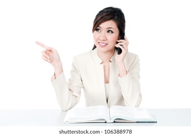 Portrait of an attractive young Asian businesswoman talking on mobile phone and pointing at copy space over white background. - Shutterstock ID 106388978