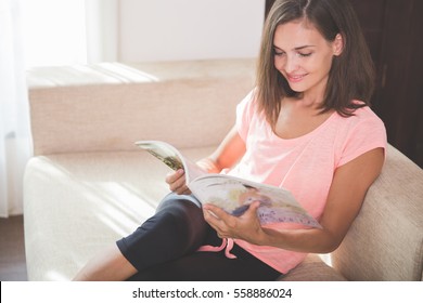 Portrait Of Attractive Young Asian Woman Reading Magazine While Sitting On A Couch