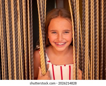 A Portrait Of An Attractive Young Caucasian Woman With Long Blond Hair In Suspenders Peeking Through The Curtains Of Her Front Door