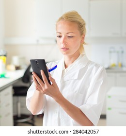 Portrait Of An Attractive, Young, Confident Female Health Care Professional In His Working Environment Making Notes On Her Smarth Phone.