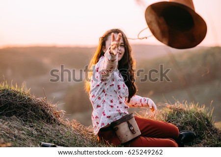 Portrait of a attractive young girl in the mountains at sunset. She resting and sitting wearing stylish fall outfit. Throws off her hat. Concept travel