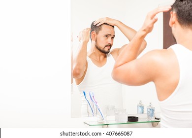 Portrait Of An Attractive Young Hispanic Man Styling His Hair In Front Of A Mirror Using Some Gel