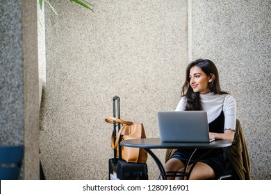 Portrait Of An Attractive Young Professional Indian Woman, Sitting At Her Desk And Working At Her Laptop. She Looks Relaxed And Happy. 