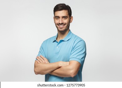 Portrait Of Attractive Young Sporty Man In Blue Polo Shirt Standing With Crossed Arms, Isolated On Gray Background