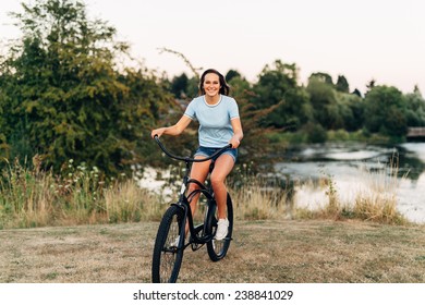 Portrait Of Attractive Young Woman In Blue Shirt With Cool Beach Cruiser Bike Riding, Smiling At Camera