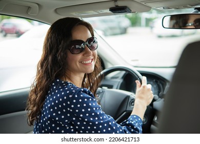 Portrait Of Attractive Young Woman In Casual Dress Looking Over Her Shoulder While Sitting Behind Steering Wheel Driving A Car