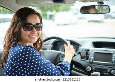 Portrait Of Attractive Young Woman In Casual Dress Looking Over Her Shoulder While Sitting Behind Steering Wheel Driving A Car