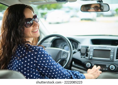 Portrait Of Attractive Young Woman In Casual Dress Looking Over Her Shoulder While Sitting Behind Steering Wheel Driving A Car