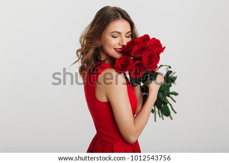 Portrait of an attractive young woman dressed in red dress holding bouquet of roses isolated over white background