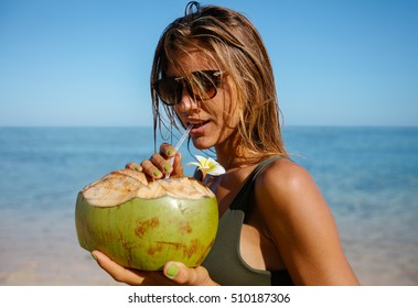 Portrait of attractive young woman drinking coconut water on the beach. Caucasian woman wearing sunglasses having fresh coconut water.