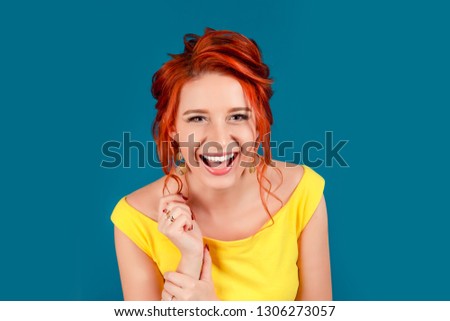 Portrait of an attractive young woman laughing hard. Caucasian person in yellow dress and beige lipstick, redhead hair up isolated on blue studio background. Expressive girl, human emotion, face