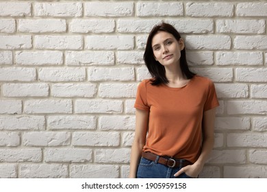 Portrait attractive young woman on white brick wall background, beautiful female wearing casual clothes orange t-shirt and blue jeans looking at camera, businesswoman or student posing for photo - Powered by Shutterstock