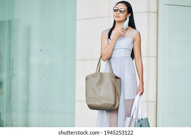 Portrait Of Attractive Young Woman In Sunglasses Taking Off Protective Mask To Have A Breath Of Fresh Air After Leaving The Store