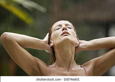 Portrait of an attractive young woman under the tropical rain, tilting her head back and feeling the rain falling on her face.