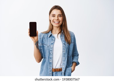 Portrait einer attraktiven jungen Frau mit weißem Lächeln, mit leerem Smartphone-Bildschirm, demonstrieren Sie eine App oder einen Online-Shopping-Shop, Studiohintergrund