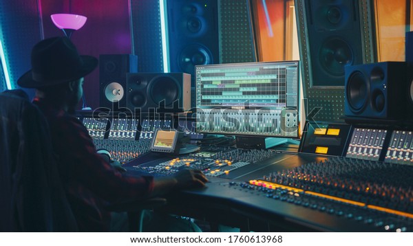 Portrait of Audio Engineer Working in\
Music Recording Studio, Uses Mixing Board Create Modern Sound.\
Successful Black Artist Musician Working at Control\
Desk.