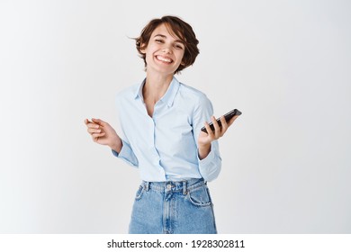 Portrait Of Authentic Happy Woman Holding Mobile Phone, Smiling And Dancing, Standing On White Background.