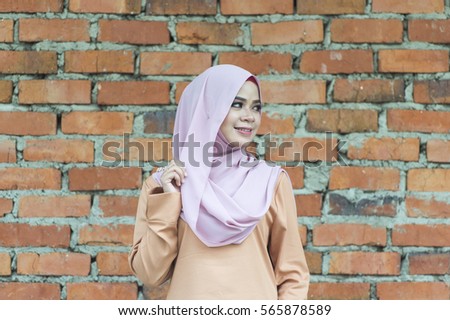 Portrait of authentic malaysian young lady in modern muslim attire reacting happily on the bricks background.