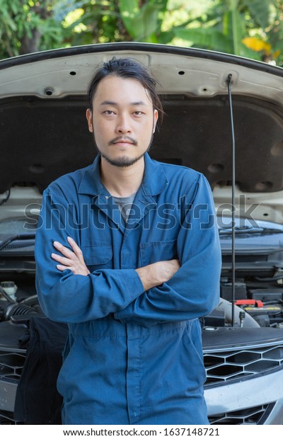 Portrait of auto mechanic in blue uniform crossed\
arms in repair shop