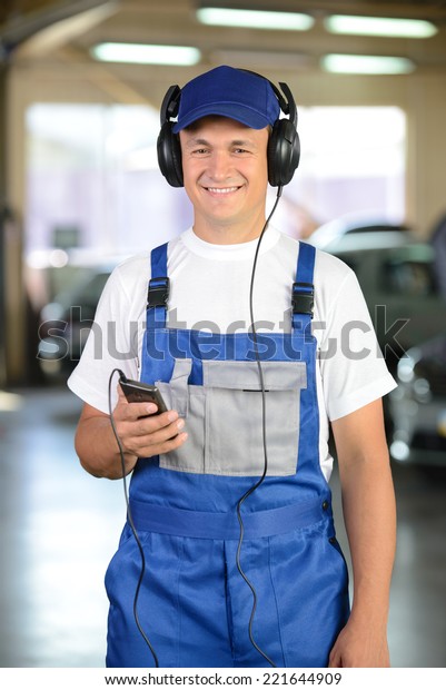 Portrait of auto mechanic, listening to music\
in headphones. Car\
background