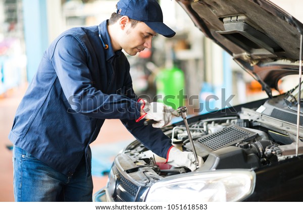 Portrait of an auto mechanicin front of a car in\
his garage