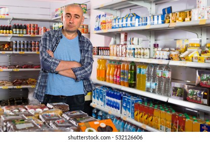 Portrait Of Average Man Standing Near Shelf With Mineral Water In Grocery
