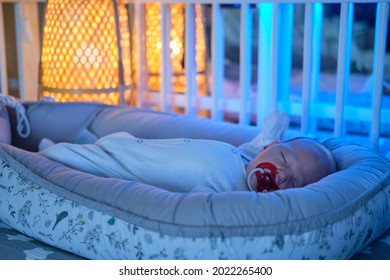 Portrait Of A Baby Boy Aged One Month Sleeping In A Crib. Caucasian Child In The Childrens Bedroom