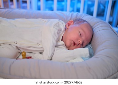 Portrait Of A Baby Boy Aged One Month Sleeping In A Crib. Caucasian Child In The Childrens Bedroom