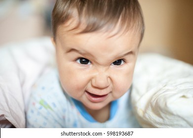 Portrait Of Baby Boy Angry, Furious, Frowning And Agressive Lying On Blanket. Funny Face Of Newborn Child