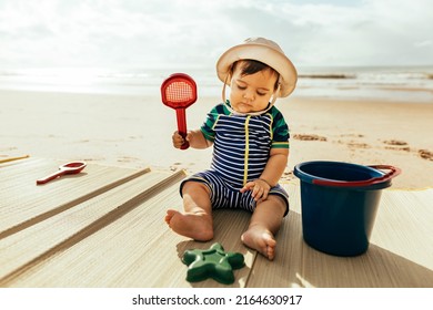 Portrait Of A Baby Boy Sitting On The Beach During Summer Vacation At Sea