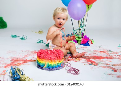 Portrait of baby girl celebrating her first birthday with gourmet cake and balloons.
