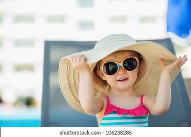 Portrait Of Baby In Hat And Glasses Sitting On Sun Bed