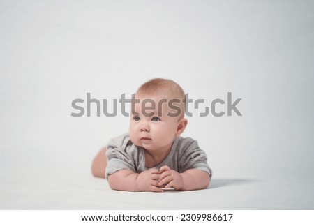 Portrait of a baby on a light background in gray clothes. The baby lies on his stomach. studio photography