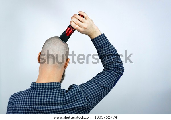 Portrait of back bald\
man head holding a trimmer in his hand. The concept of hair loss\
and hair\
transplantation