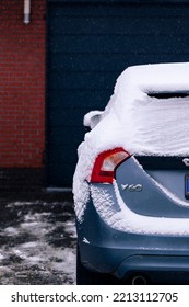 A Portrait Of The Back Of A Blue Car Covered In White Snow During Winter Parked On A Driveway. The Driver Will Have To Clear The Windows Before Driving Or Will Have To Wait For The Snow To Melt.