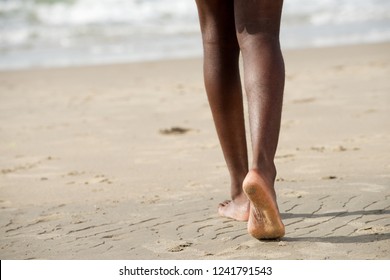 Portrait Of Back Of Young Black Man Legs Walking Barefoot On Beach Towards Water 