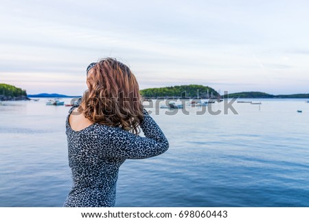 Portrait of back of young woman touching hair on edge of dock in Bar Harbor, Maine at sunset