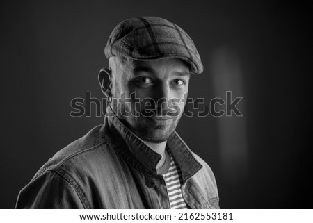 Portrait in balck and white colores trendy man in cap looking at camera with slight smile and calmness while expressing kindness in his eyes