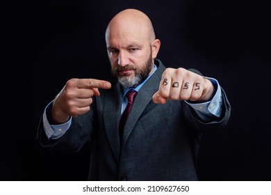 Portrait of a bald business man in suit on dark background. Right hand points to sign boss on his fist. The model is in his 40s, grey and dark hair beard. Showing authority and power concept.