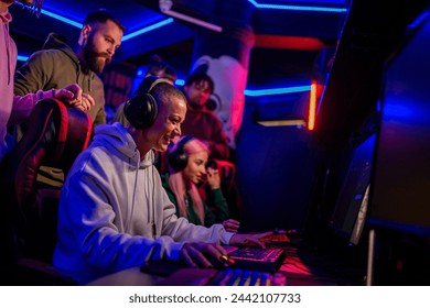 Portrait of a bald female gamer sitting in front of a computer in cyber club and playing a video game while her team is cheering for her. Esport streaming game online. Friends playing video games. - Powered by Shutterstock