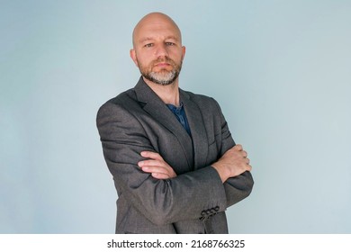 Portrait Of A Bald Man In Grey Suit On Light Blue Background. Male Model In His 40s With Grey Beard. Middle Age Professional. Looking At The Viewer.