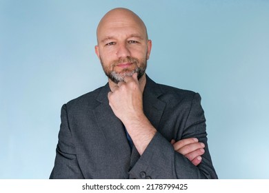 Portrait Of A Bald Man In Grey Suit On Light Blue Background. Male Model In His 40s With Grey Beard. Middle Age Professional. Looking At The Viewer.