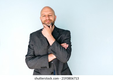 Portrait Of A Bald Man In Grey Suit On Light Blue Background. Male Model In His 40s With Grey Beard. Middle Age Professional. Looking At The Viewer.